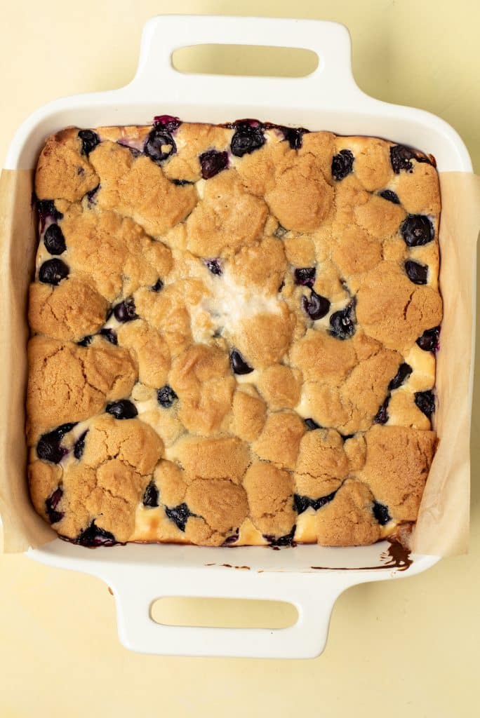 baked blueberry cheesecake sugar cookie bars in a parchment paper lined baking dish