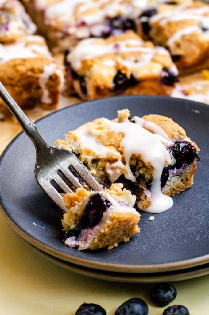 a black fork with a piece of blueberry cream cheese topped sugar cookie bars on a dark blue dessert plate