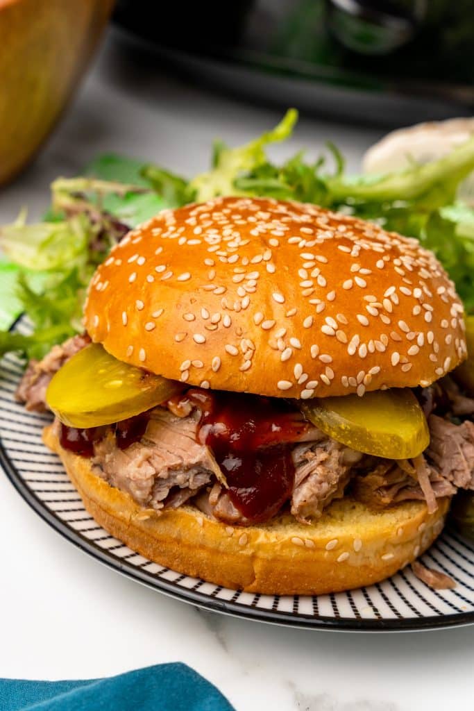 crockpot pulled pork topped with barbecue sauce on a sesame seed bun