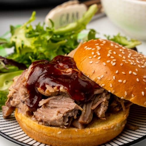 crockpot pulled pork topped with barbecue sauce on a sesame seed bun