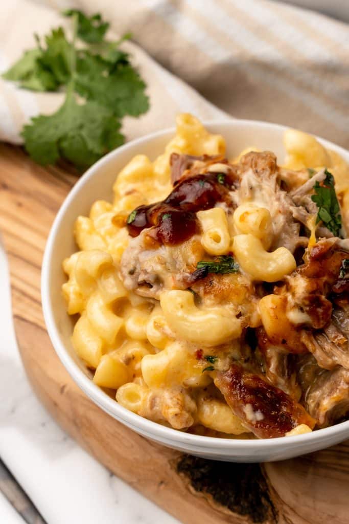 pulled pork mac and cheese in a white bowl topped with barbecue sauce and cilantro leaves