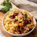 pulled pork mac and cheese in a white bowl topped with barbecue sauce and cilantro leaves