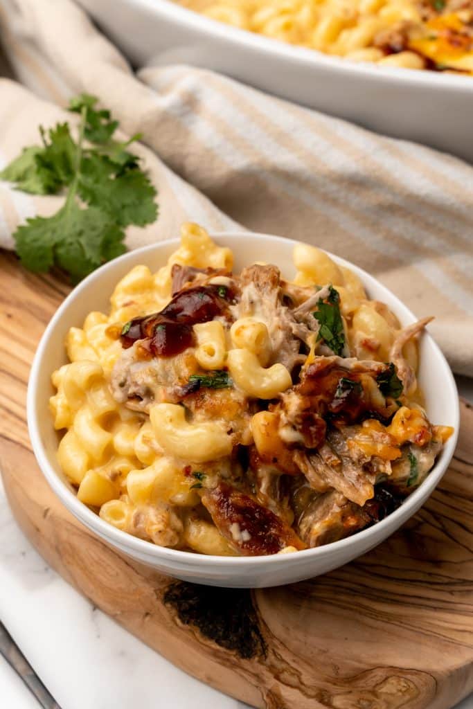 pulled pork mac and cheese in a white bowl topped with barbecue sauce and cilantro leaves