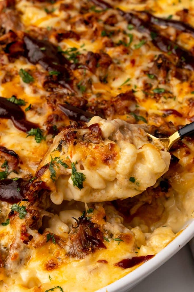 a spoon scooping pulled pork mac and cheese out of a white casserole dish