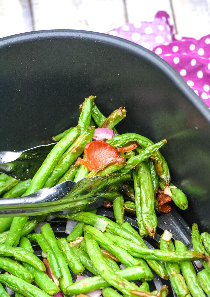 a pair of silver tongs holding air fryer green beans and bacon