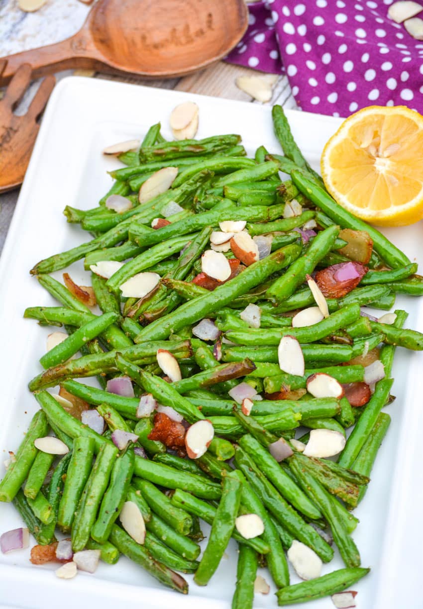 air fryer green beans on a white platter with slivered almonds and bacon crumbles