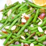 air fryer green beans on a white platter with slivered almonds and bacon crumbles