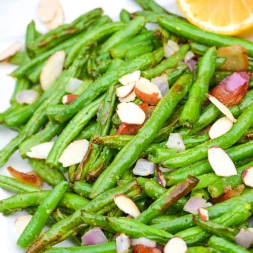 air fryer green beans on a white platter with slivered almonds and bacon crumbles