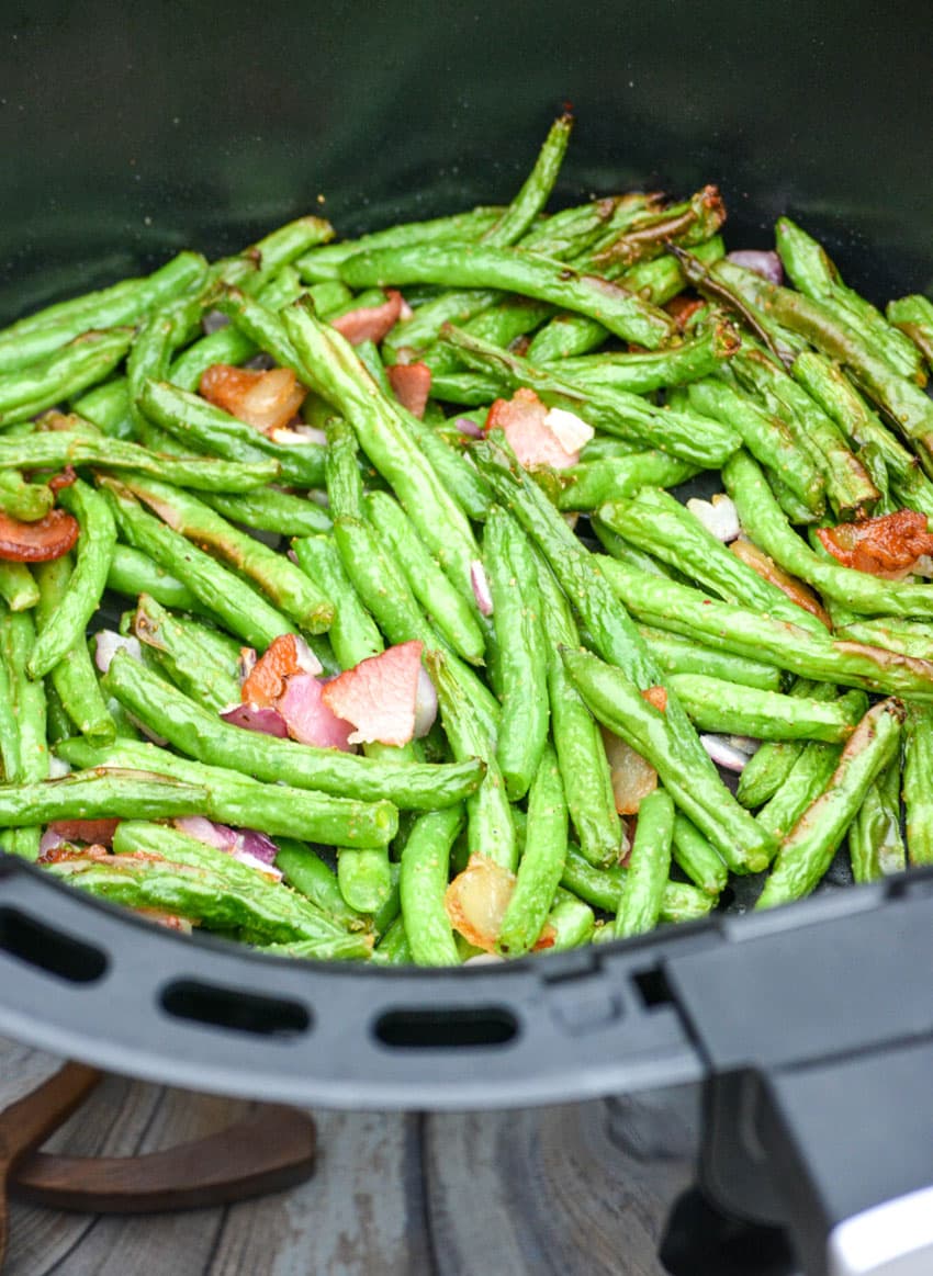 tender green beans with red onion and bacon in the basket of an air fryer