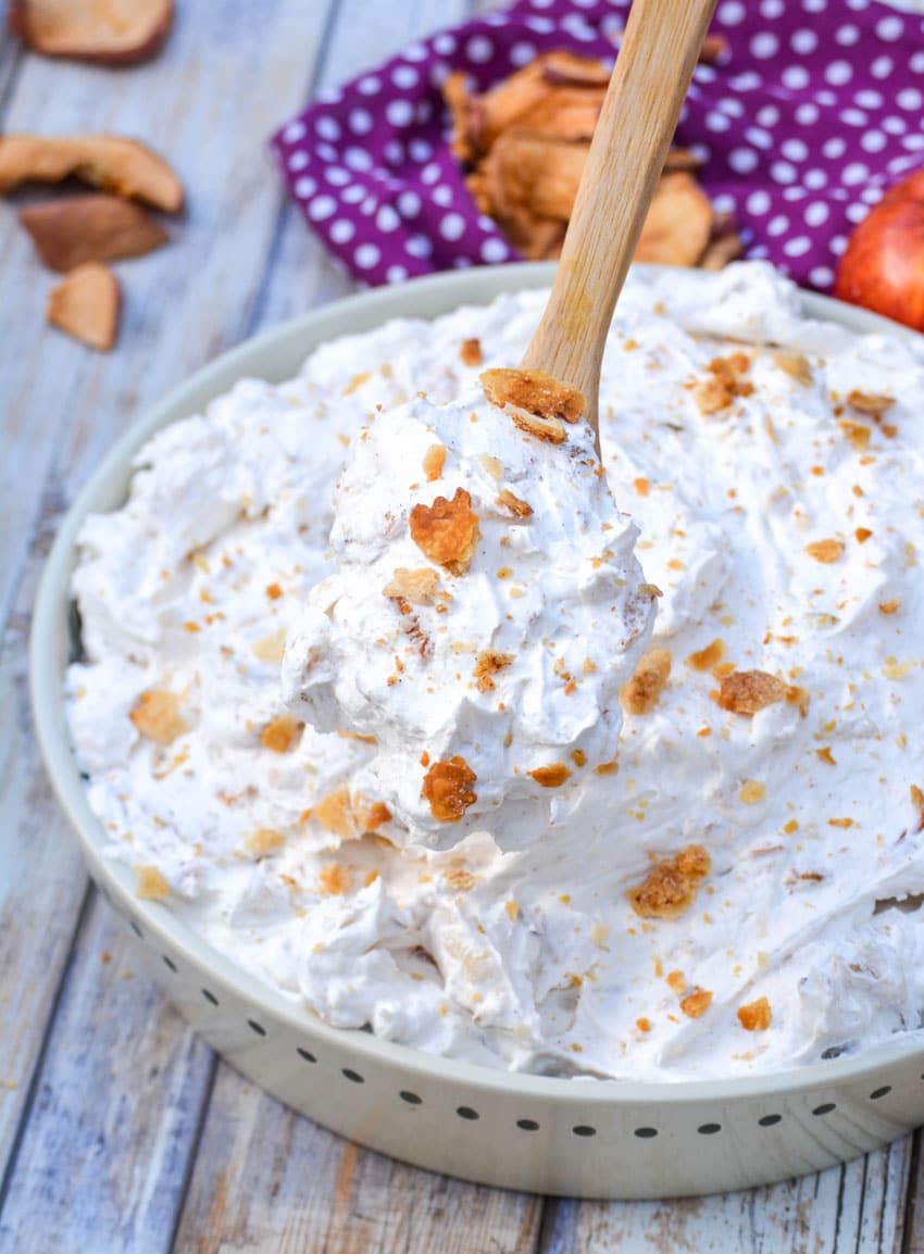 a wooden spoon lifting a scoop of apple pie fluff salad out of a shallow white bowl