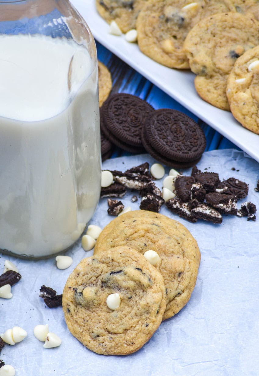 cookies and cream oreo pudding cookies with white chocolate chips on a piece of parchment paper next to a glass milk jar