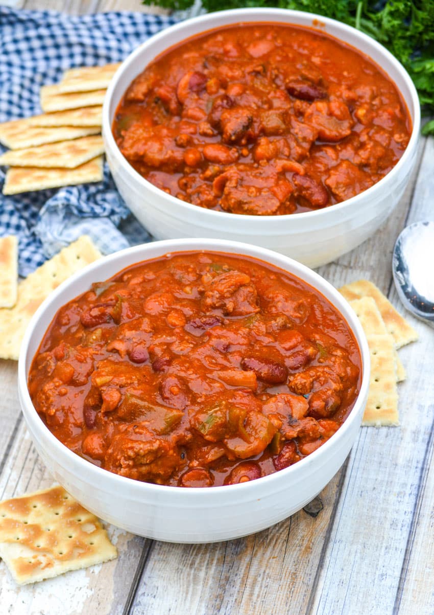 two white bowls filled with hamburger chili surrounded by saltine crackers
