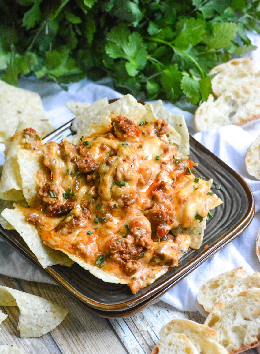 crispy tortilla chips on a brown appetizer plate topped with cheesy queso fundido dip