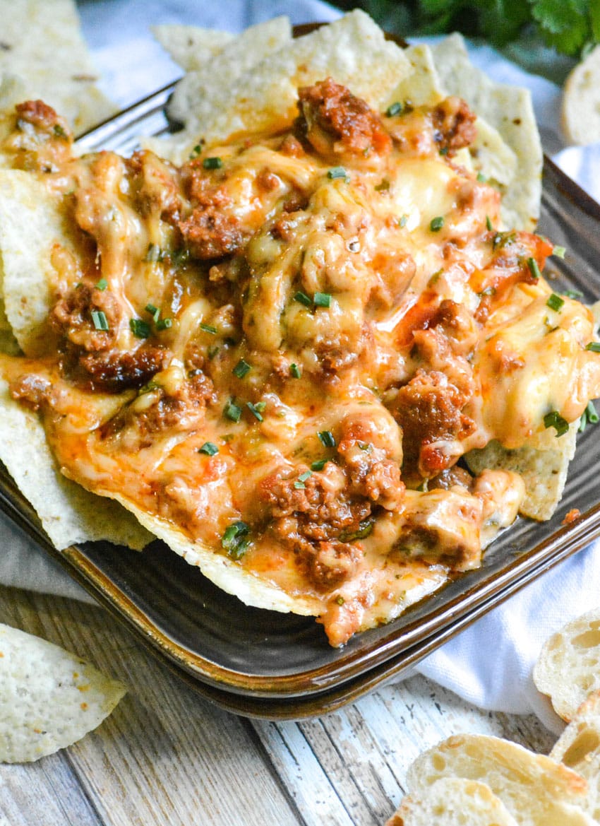 crispy tortilla chips on a brown appetizer plate topped with cheesy queso fundido dip
