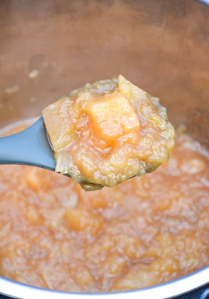 a spoon holding up a scoop of apple pie filling above the liner of an instant pot pressure cooker