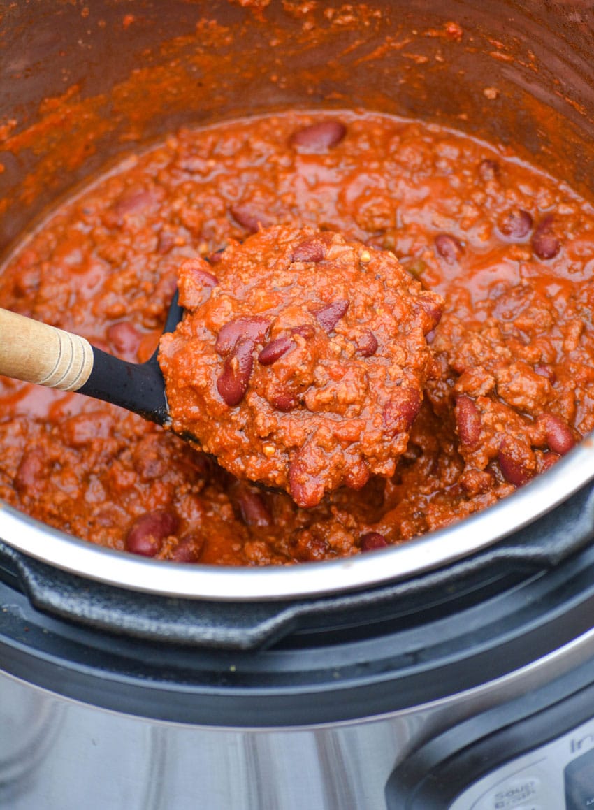 a wooden ladle lifting a scoop of chili out of an instant pot pressure cooker