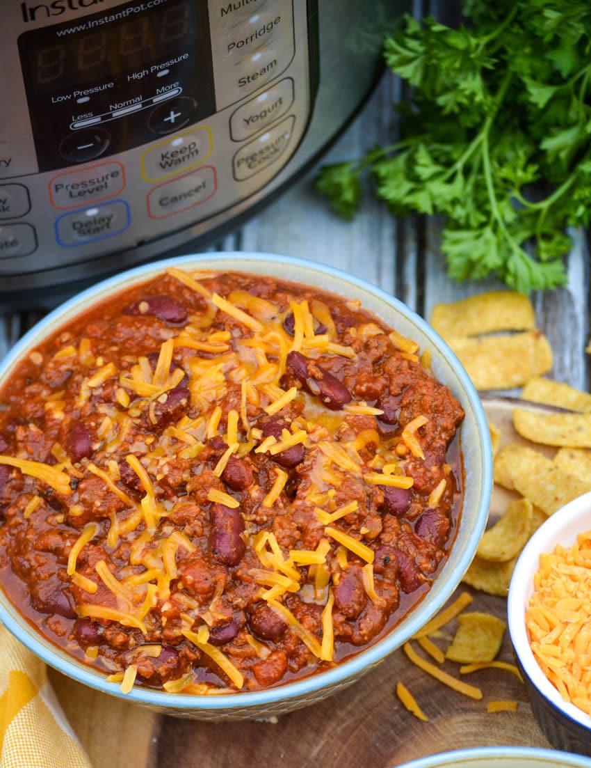 a bowl of Instant Pot chili topped with shredded cheddar on a wooden cutting board