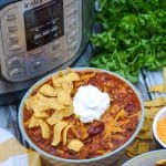 a bowl of Instant Pot chili topped with shredded cheddar on a wooden cutting board