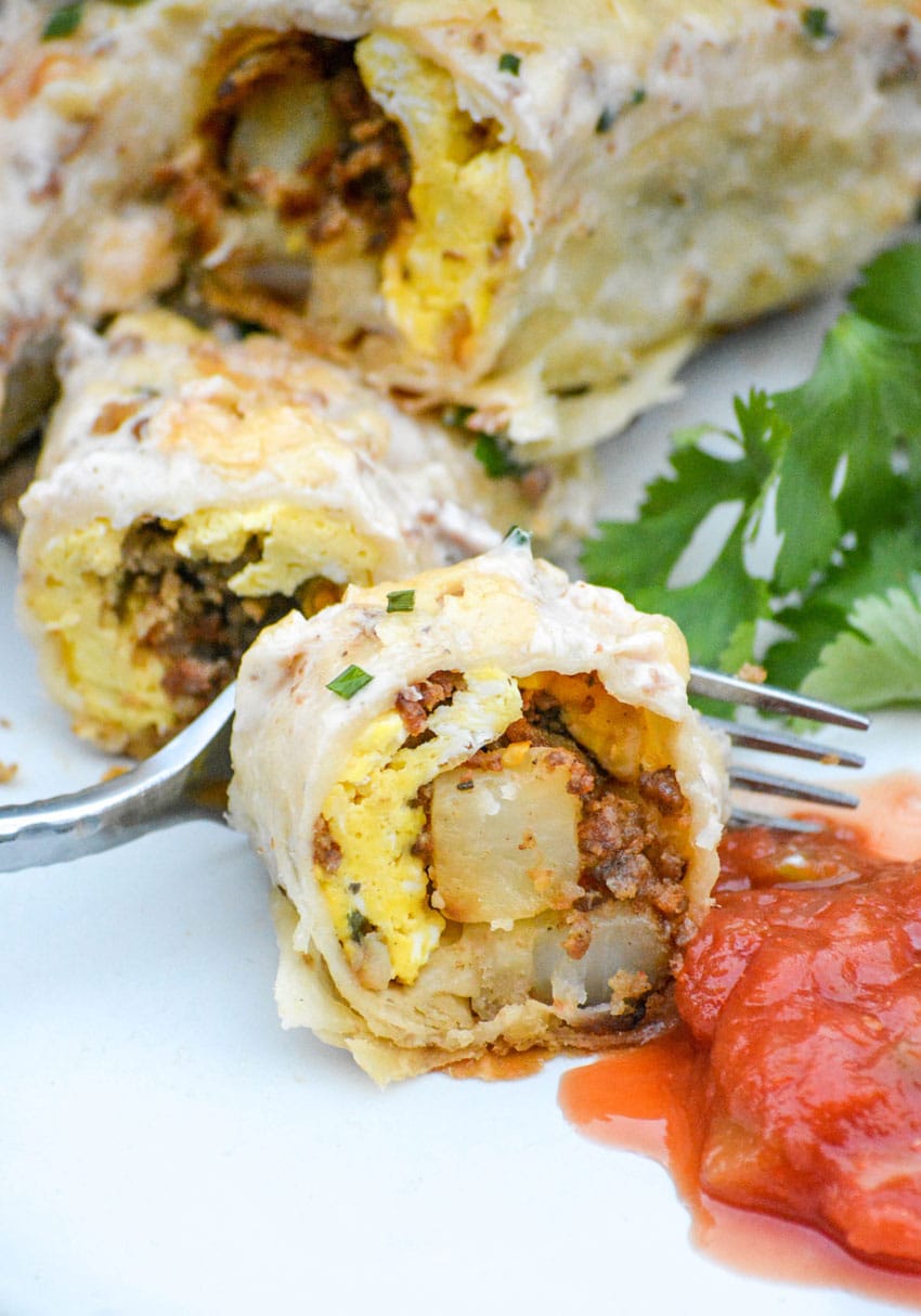 pieces of a breakfast enchilada on a white plate with salsa next to a silver fork