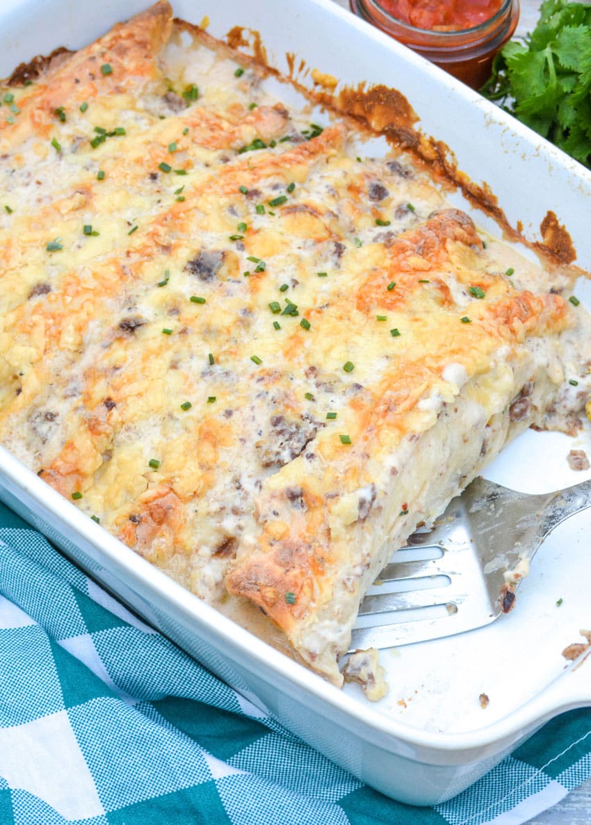 sausage gravy breakfast enchiladas in a white casserole dish with a silver spatula
