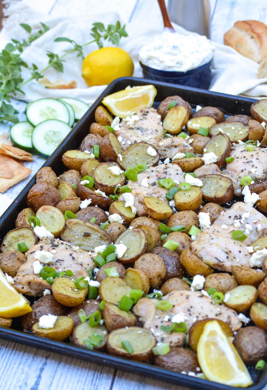 sheet pan greek chicken and potatoes topped with sliced green onions and crumbled feta cheese