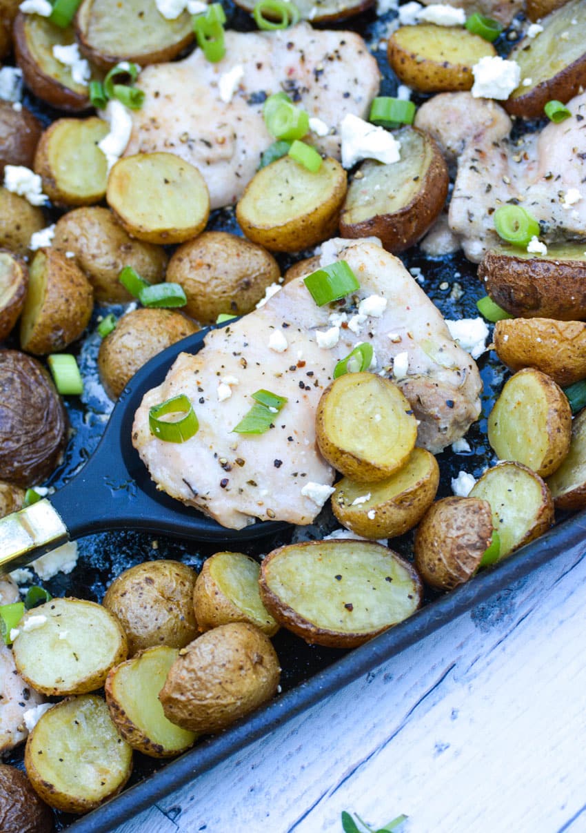 sheet pan greek chicken and potatoes topped with sliced green onions and crumbled feta cheese