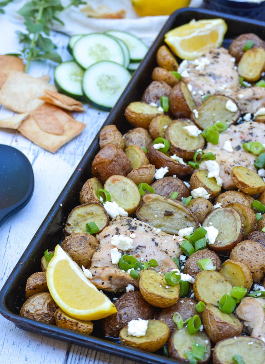 sheet pan greek chicken and potatoes topped with sliced green onions and crumbled feta cheese