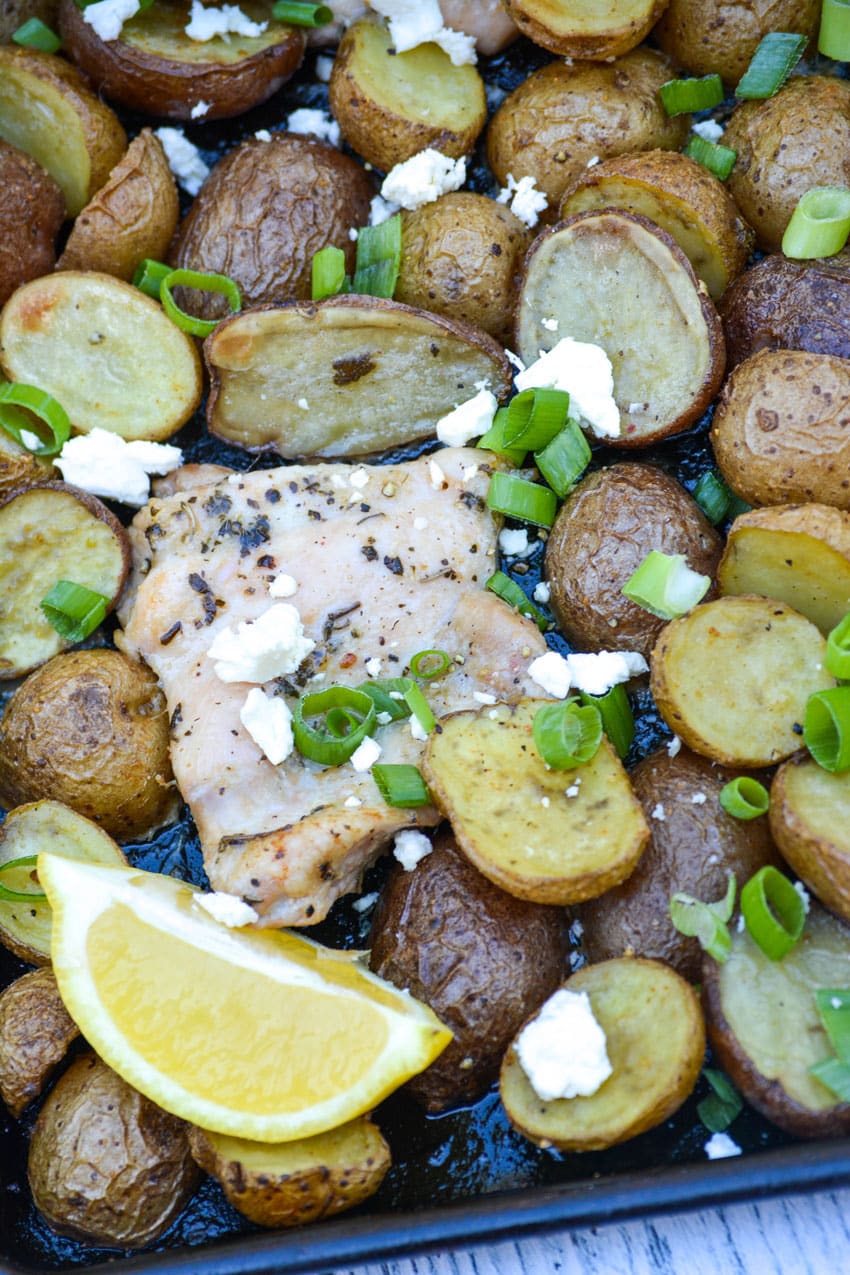 lemon feta sheet pan chicken and potatoes topped with sliced green onions and crumbled feta cheese
