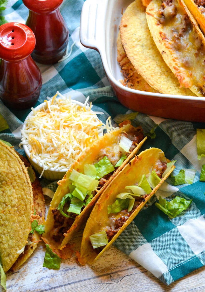 lettuce topped sloppy joe tacos sitting on a blue and white checkered cloth napkin