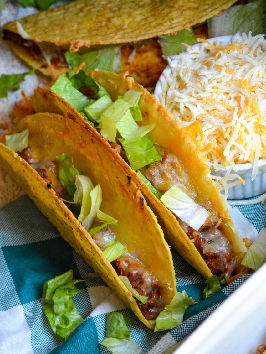 lettuce topped sloppy joe tacos sitting on a blue and white checkered cloth napkin