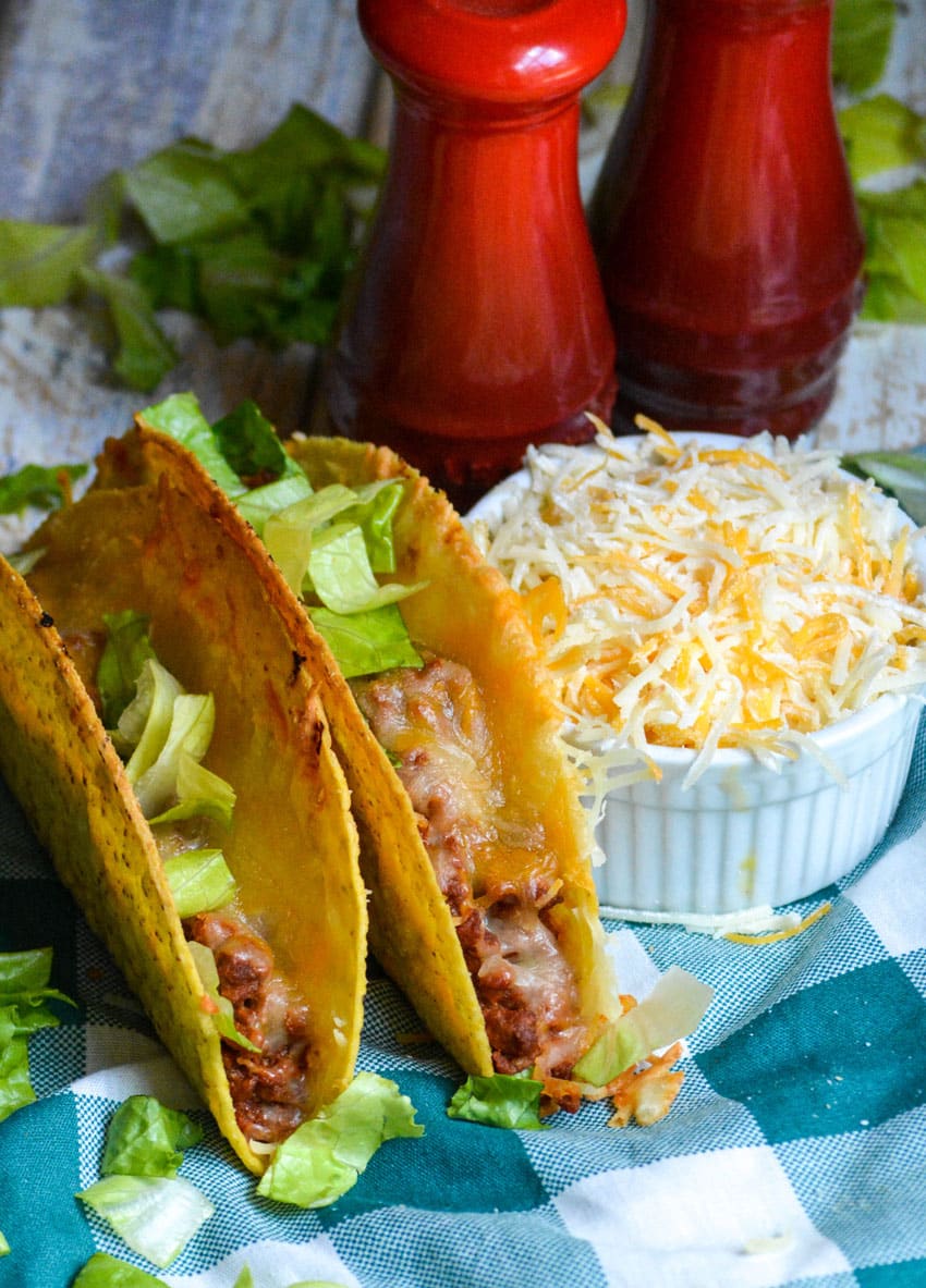 lettuce topped sloppy joe tacos sitting on a blue and white checkered cloth napkin