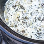 slow cooker spinach and artichoke dip in the black bowl of a crockpot