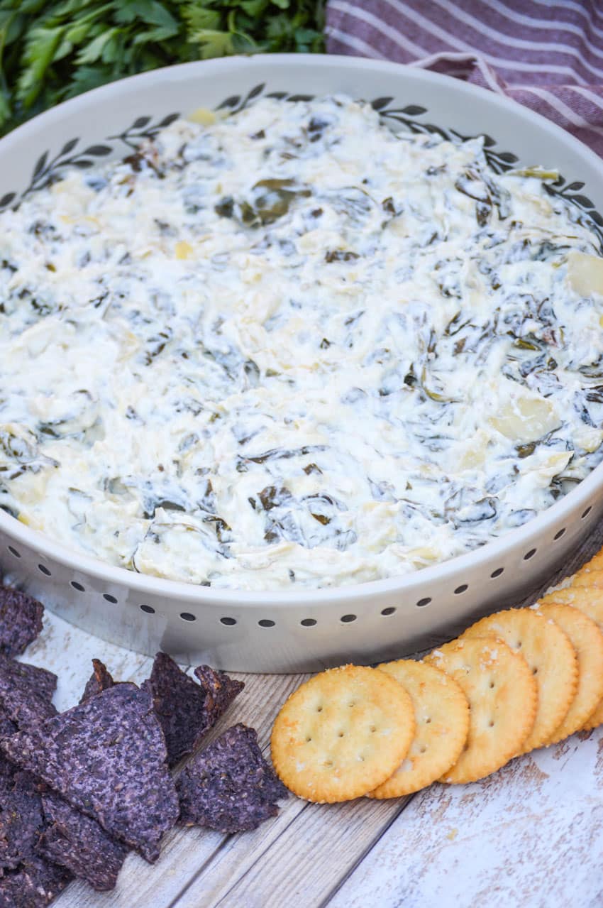 slow cooker spinach and artichoke dip in a shallow serving dish surrounded by blue corn tortilla chips and ritz crackers