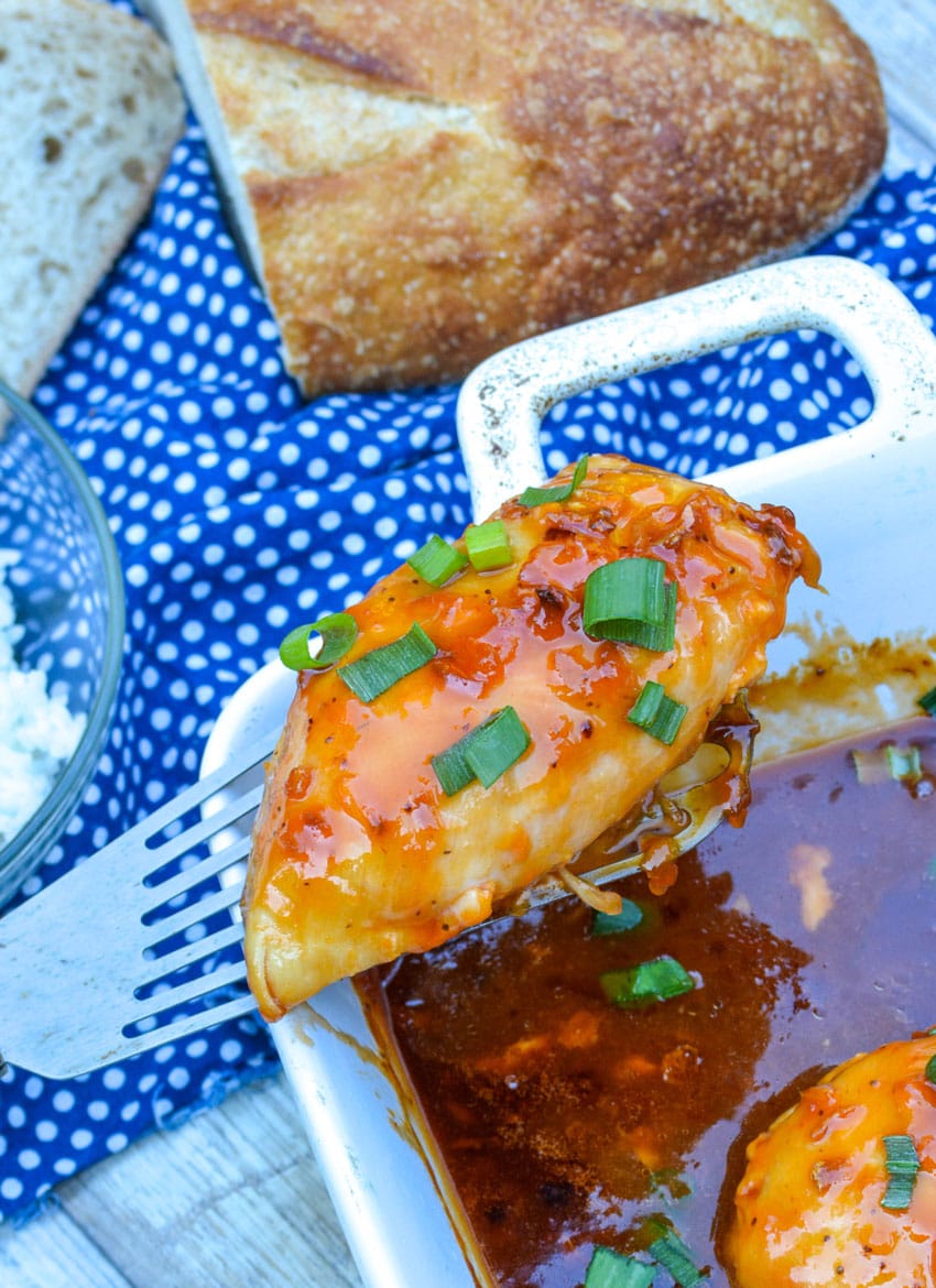 a spatula lifting a piece of baked russian chicken out of a white casserole dish