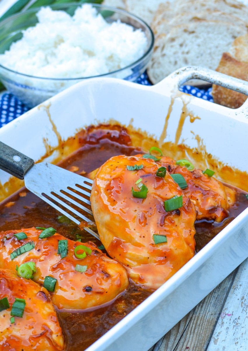 a spatula lifting a piece of baked russian chicken out of a white casserole dish
