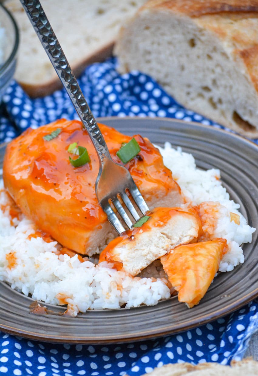 a silver fork stuck in a saucy russian dressing coated chicken breast on a bed of white rice on a brown plate