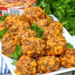 cheesy sausage stuffing balls on a white platter with fresh parsley leaves