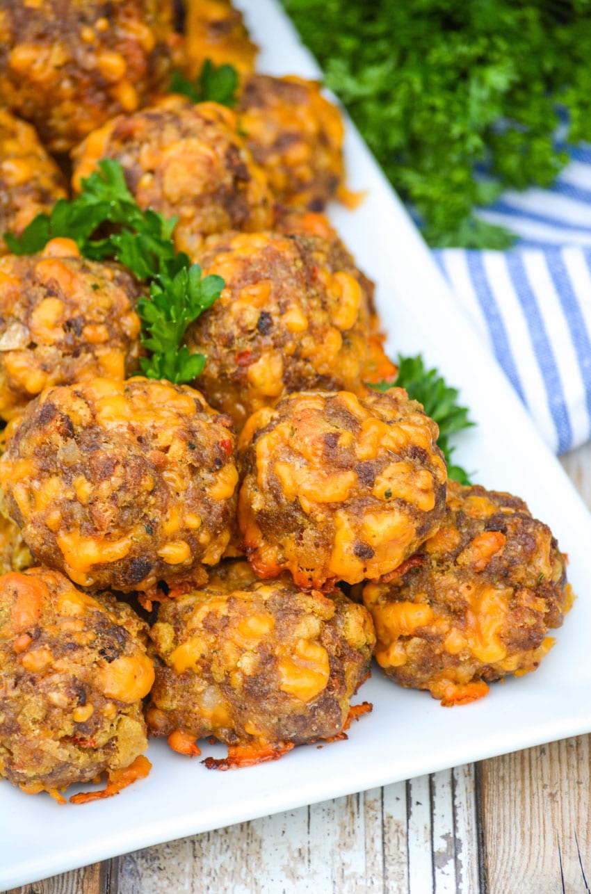 cheesy sausage stuffing balls on a white platter with fresh parsley leaves