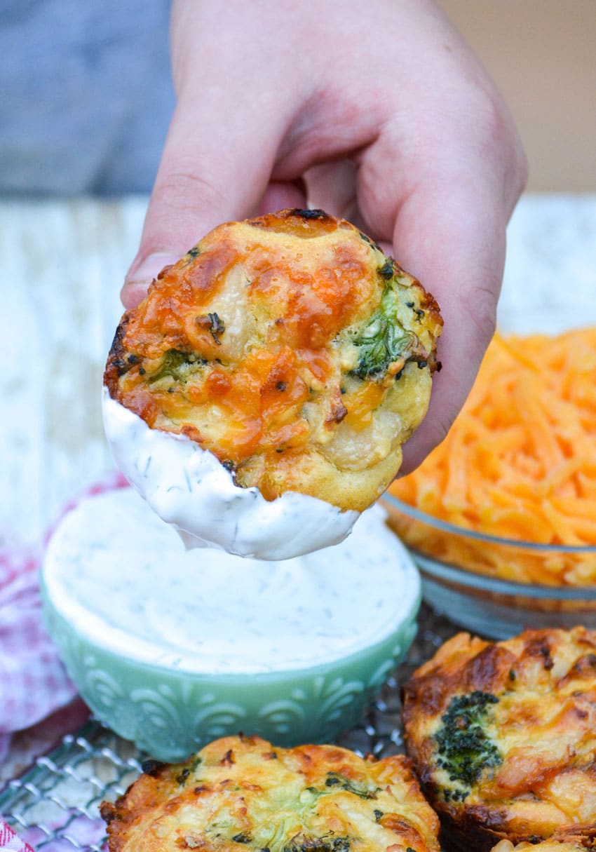 a hand holding up a cheesy chicken broccoli hand pie dipping in dill sour cream sauce