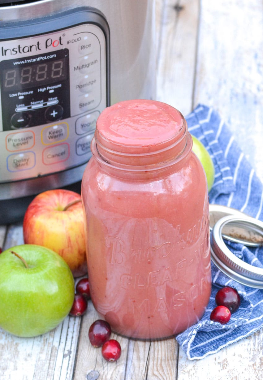 a mason jar filled with instant pot cranberry applesauce sitting in from of a pressure cooker