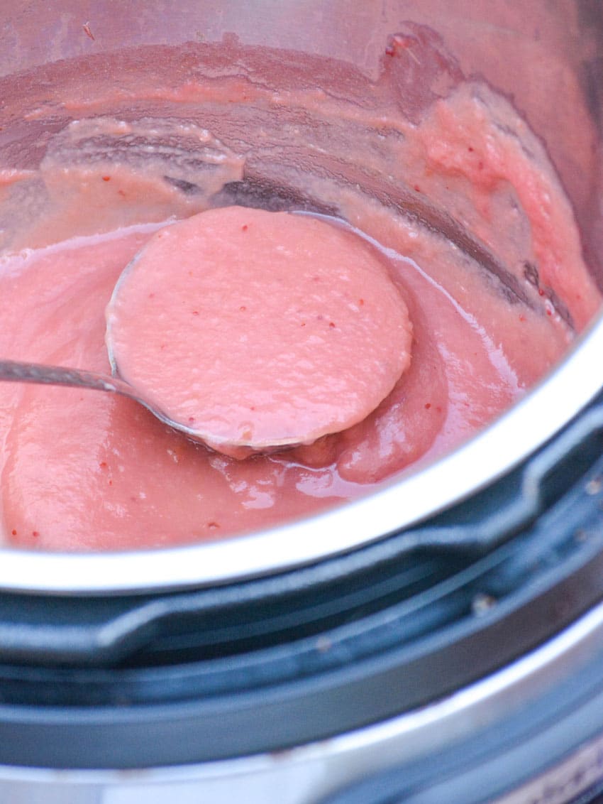 a silver ladle scooping cranberry applesauce from the liner of an instant pot