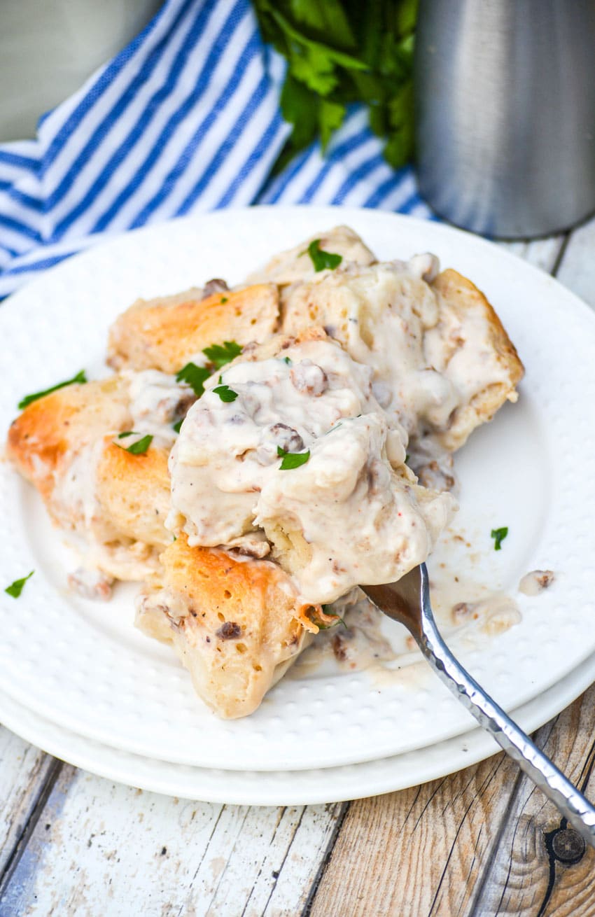 a fork stuck in a pile of sausage gravy and biscuits casserole on a white plate
