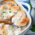 a wooden spoon in a sausage gravy and biscuits casserole in a white dish
