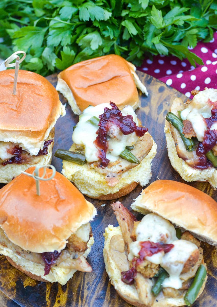 cheesy sliders stuffed with thanksgiving leftovers sit on a small wooden cutting board