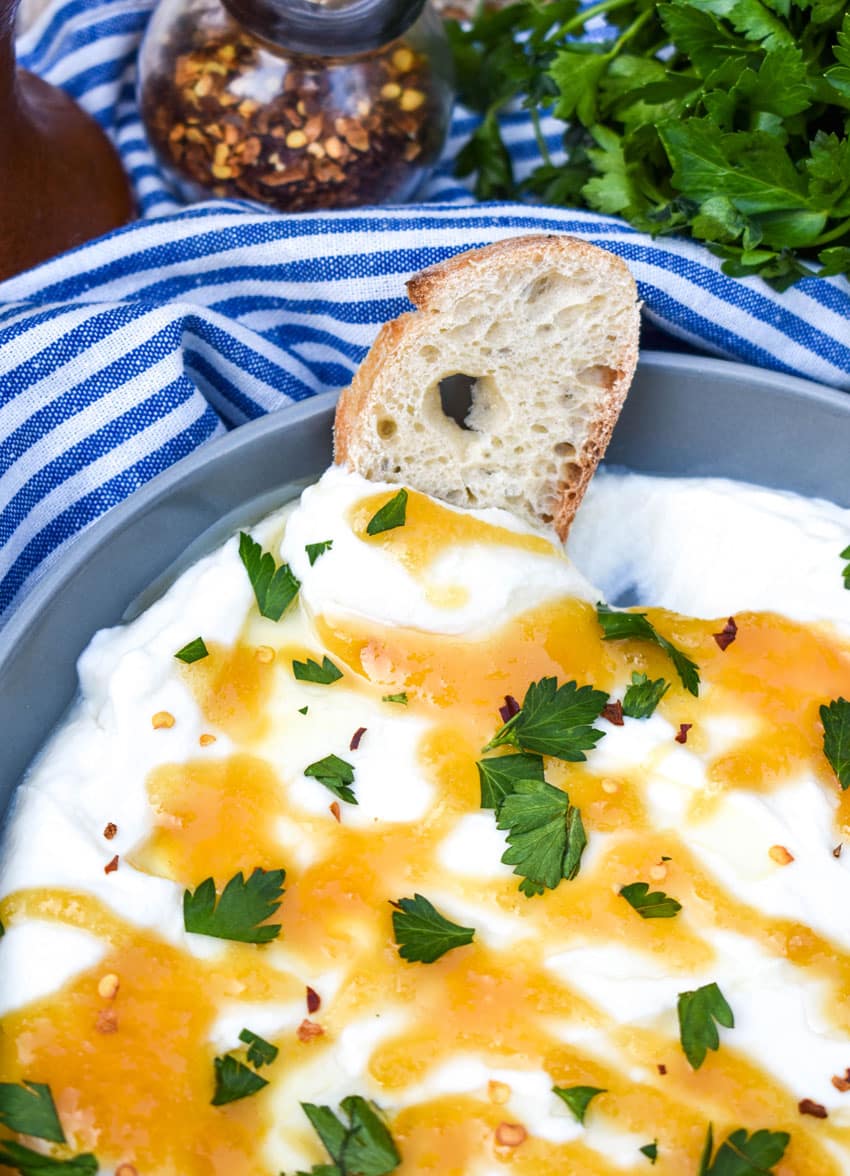 a baguette slice dipped in a shallow bowl filled with freshly whipped ricotta cheese dip topped with honey and fresh herbs