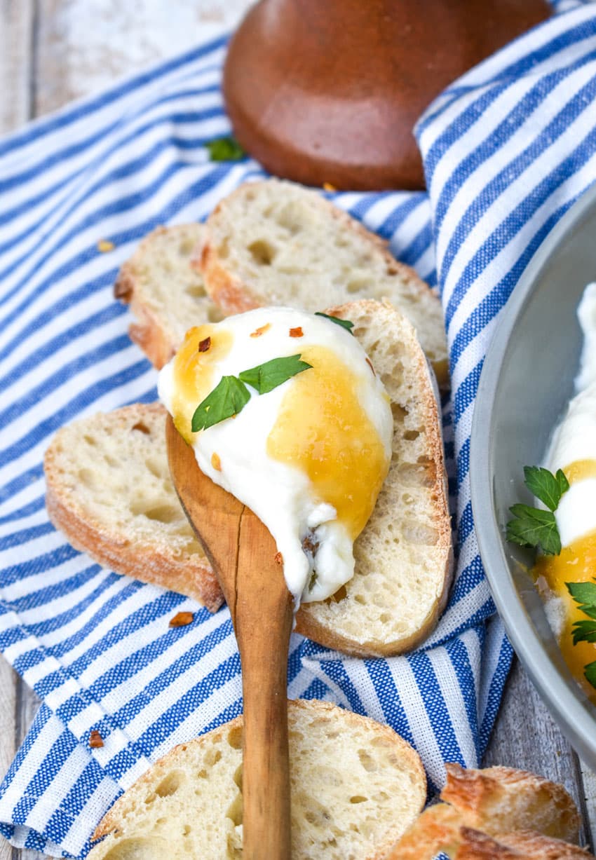 a wooden spoon resting on a baguette slice topped with whipped ricotta cheese dip spread