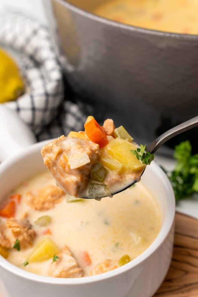 a black spoon with salmon chowder with canned salmon held up over a white soup bowl