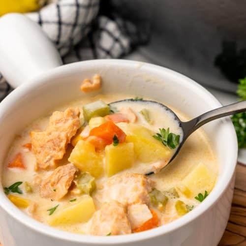a black spoon in a white bowl filled with canned salmon chowder