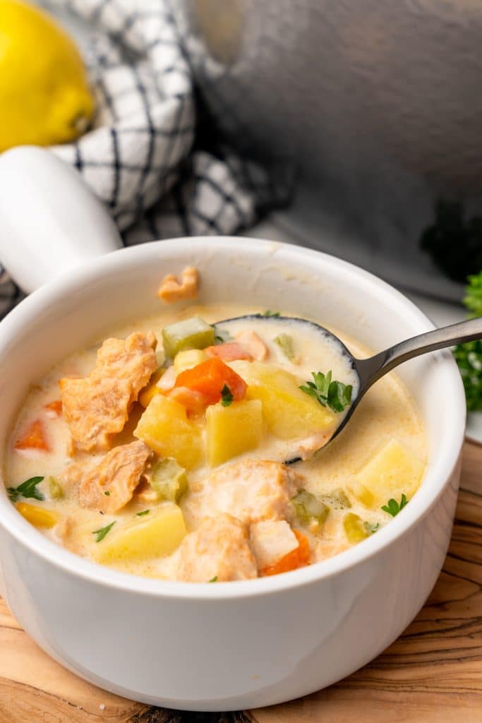 a black spoon in a white bowl filled with canned salmon chowder