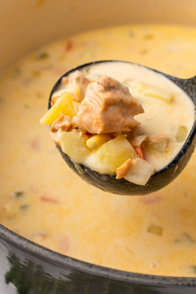 a black ladle holding up a scoop of canned salmon chowder